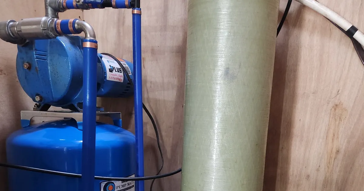 Shallow well jet pump mounted on a blue diaphragm pressure tank beside a water treatment tank in a basement serviced by EZ-CO Plumbing