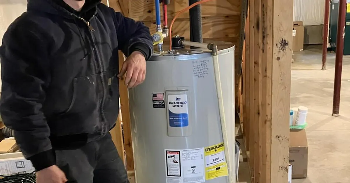 EZ-CO plumber beside a newly installed Bradford White electric water heater in a basement